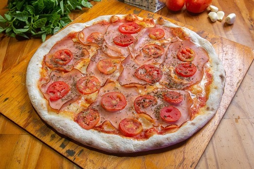 Frisch gebackene Pizza mit Schinken und Tomaten auf Holzbrett bei Mama Rosa Graz